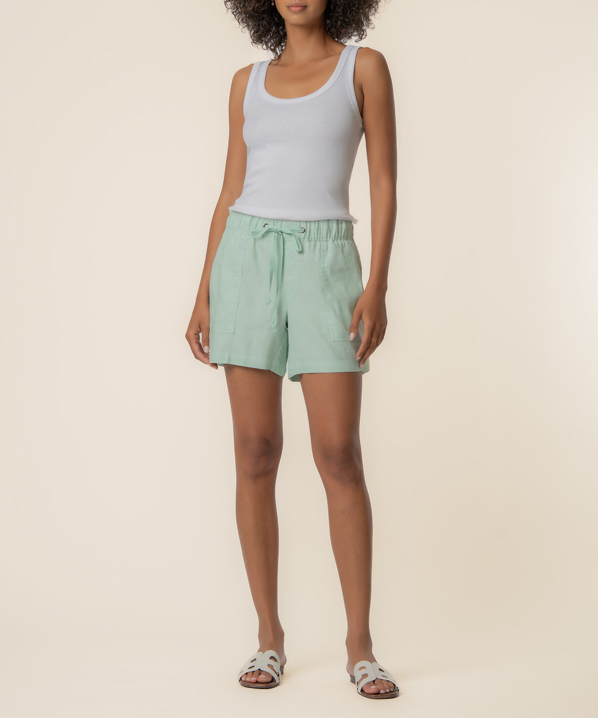 Seafoam green linen shorts with drawstring waist and side pockets, worn with white sleeveless tank top.