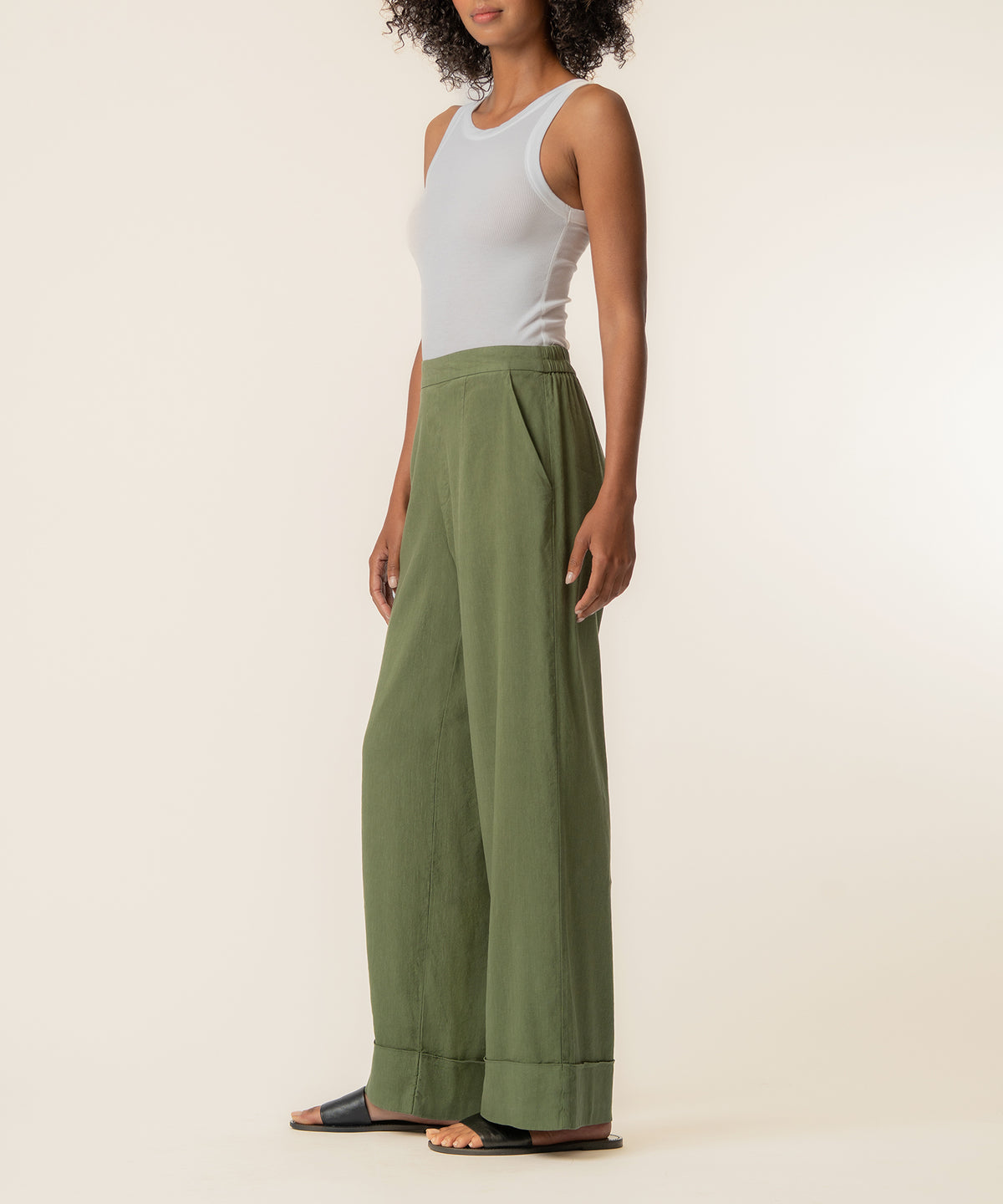 Woman wearing white sleeveless tank top and sage green high-rise wide-leg linen pants with cuffed hem.