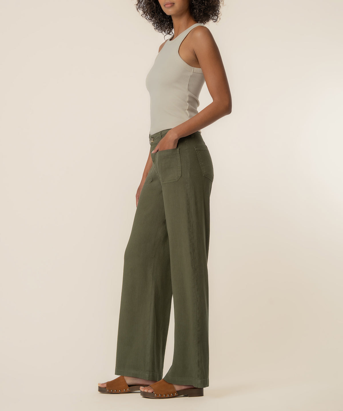 Woman wearing a cream sleeveless tank top and forest green high-rise wide-leg linen pants with studded sandals.