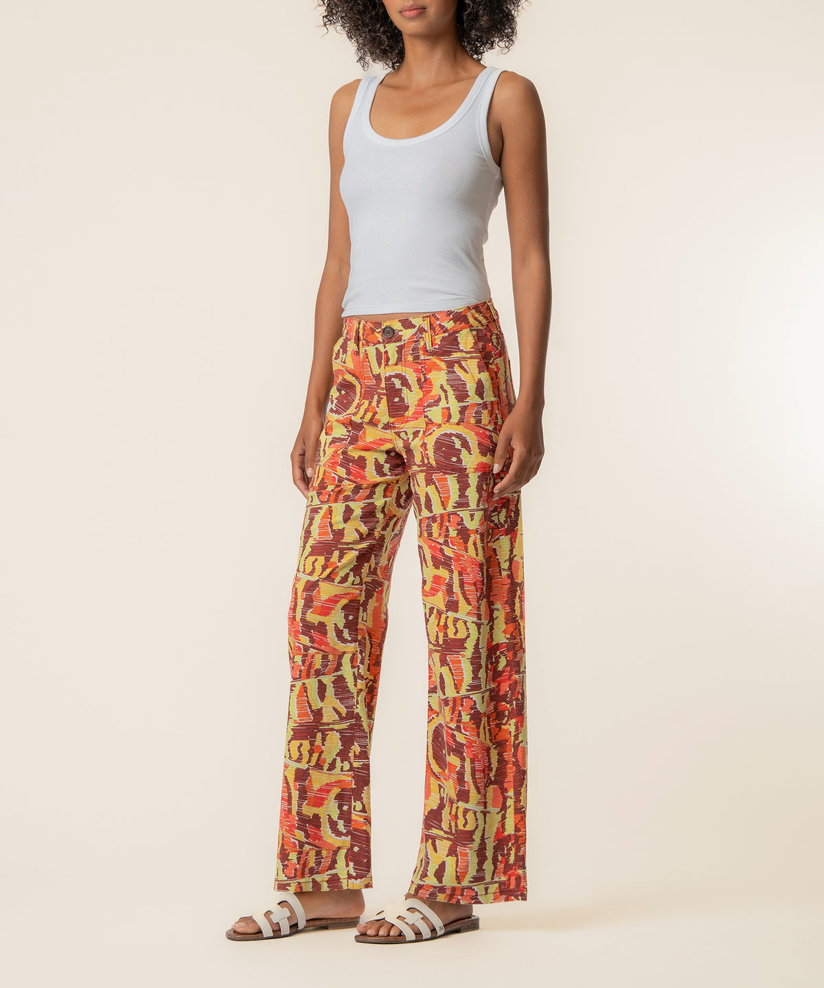 Woman wearing light blue sleeveless tank top and high-waist straight-leg linen pants in wine and yellow abstract print.