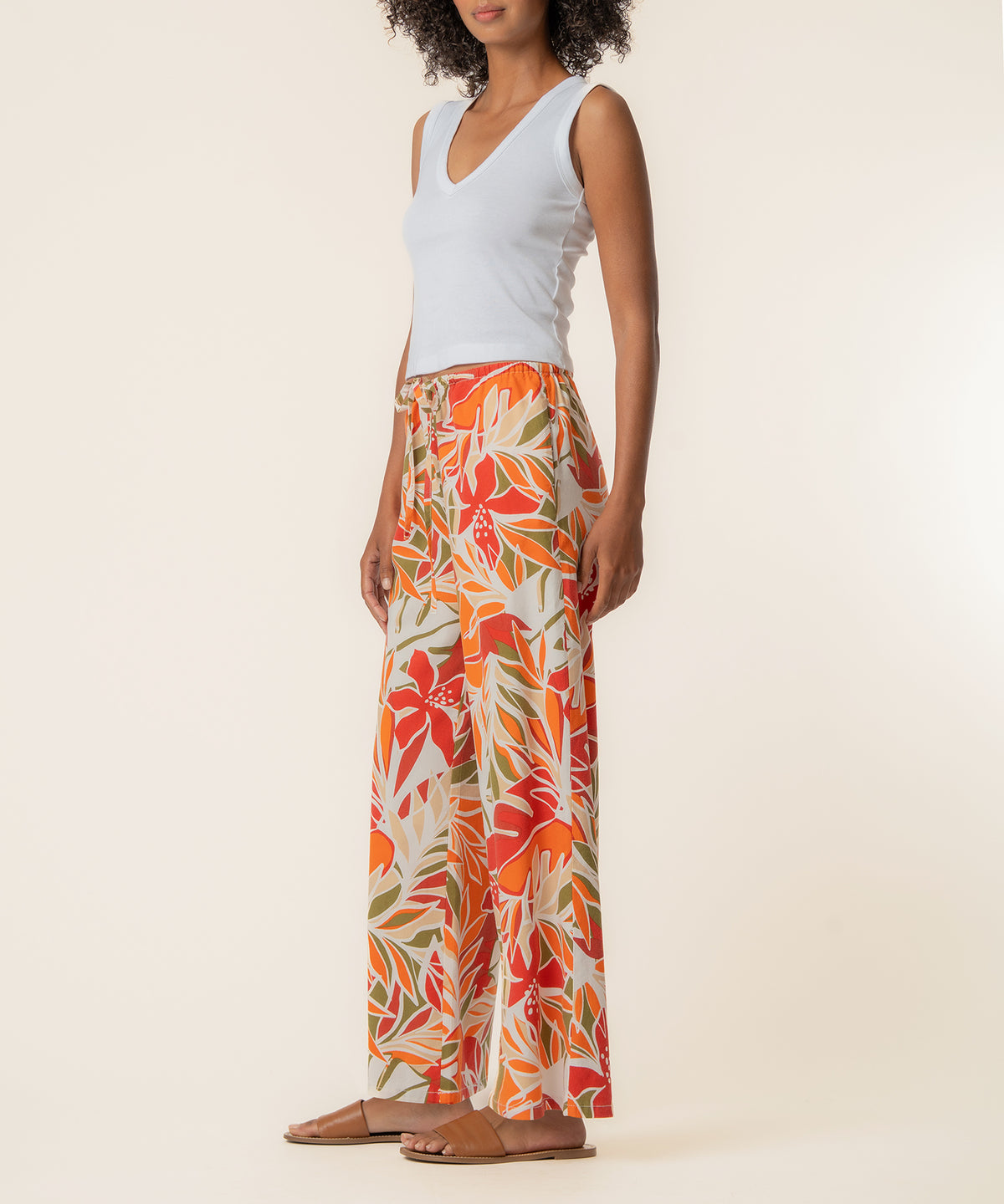 Woman wearing white sleeveless v-neck top and red-orange linen wide-leg pants with leaf print pattern.