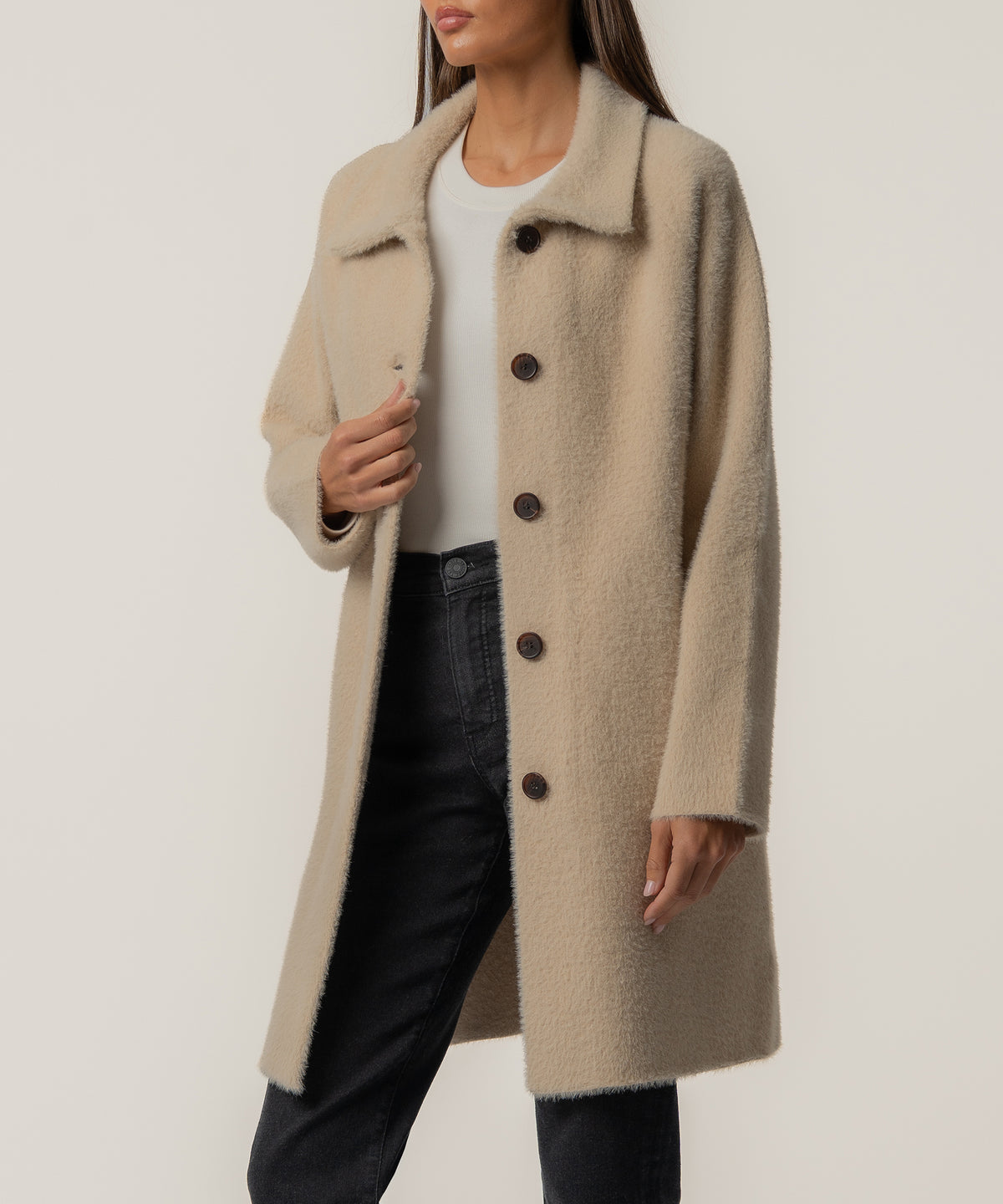 Oatmeal long sweater jacket with collar and dark button front closure worn over white tee and black pants.