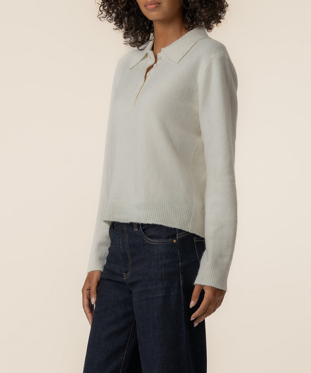 Cream-colored polo sweater with ribbed cuffs and hem, worn with dark denim jeans.