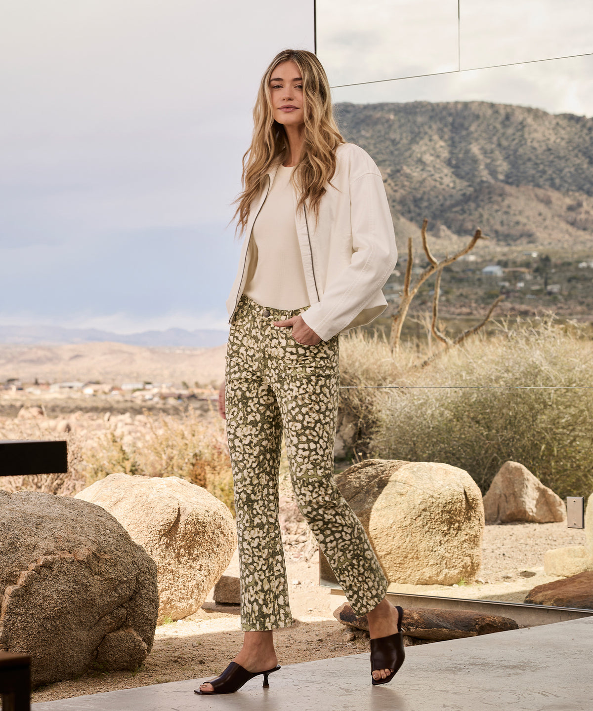 Woman wearing dark olive high-rise ankle flare pants with a cream jacket and black slide sandals.