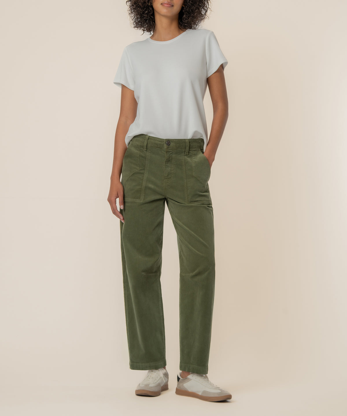Woman wearing light gray t-shirt and olive green high-rise barrel corduroy pants with white sneakers.
