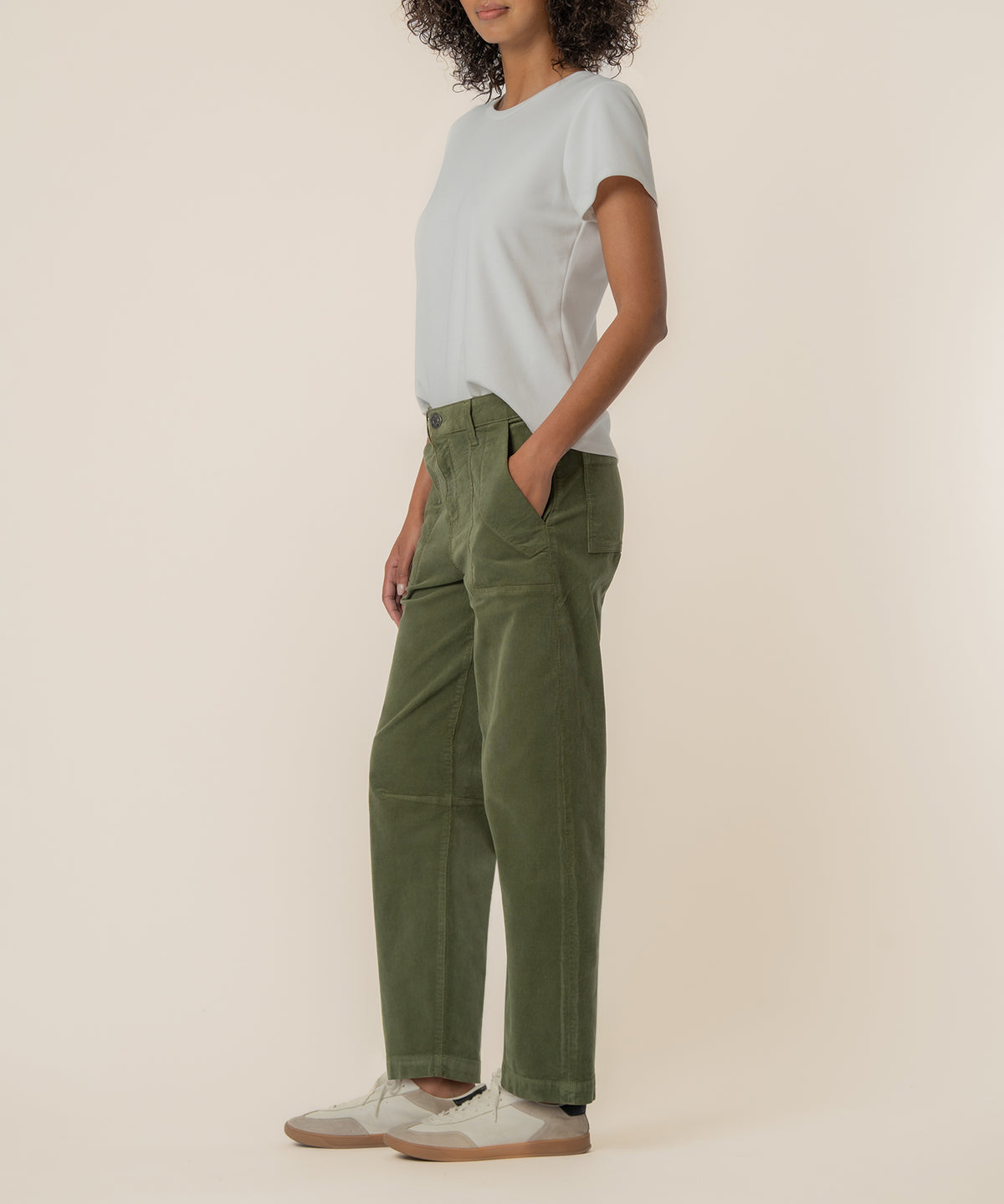 Woman wearing light gray t-shirt and high-rise olive green corduroy barrel pants with cream sneakers.