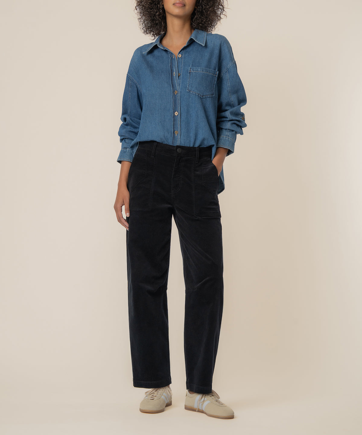 Black corduroy high-rise barrel pants with button fly and front pockets, worn with blue denim shirt.