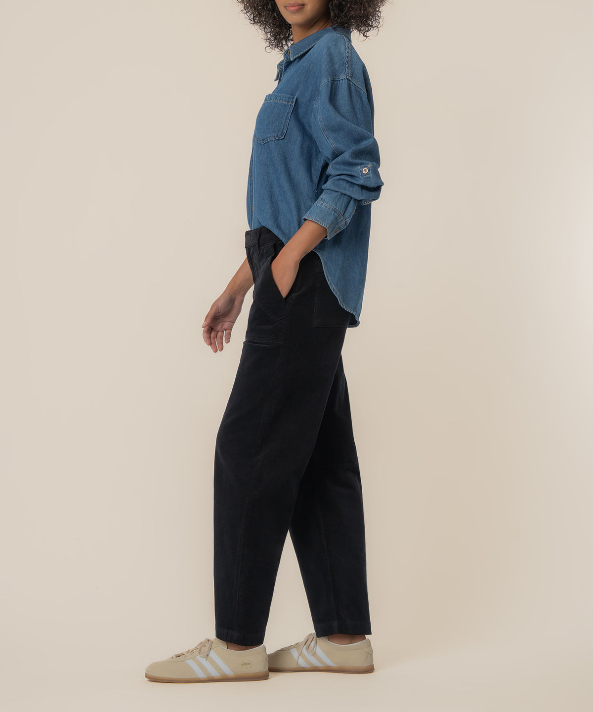 Black corduroy high-rise barrel pants with side pockets, worn with blue denim shirt.