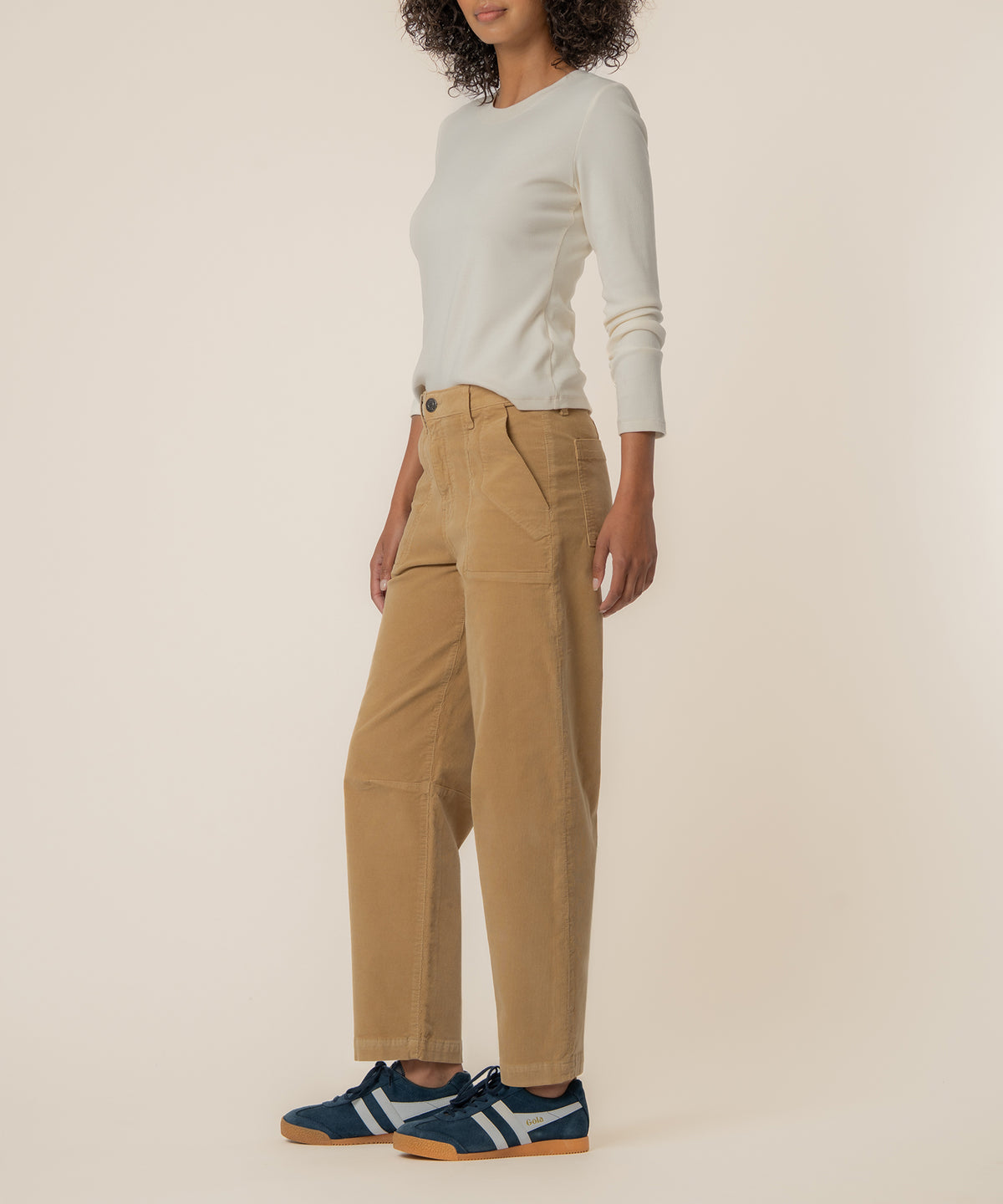 Woman wearing khaki corduroy high-rise barrel pants with cream long-sleeve top and navy sneakers.