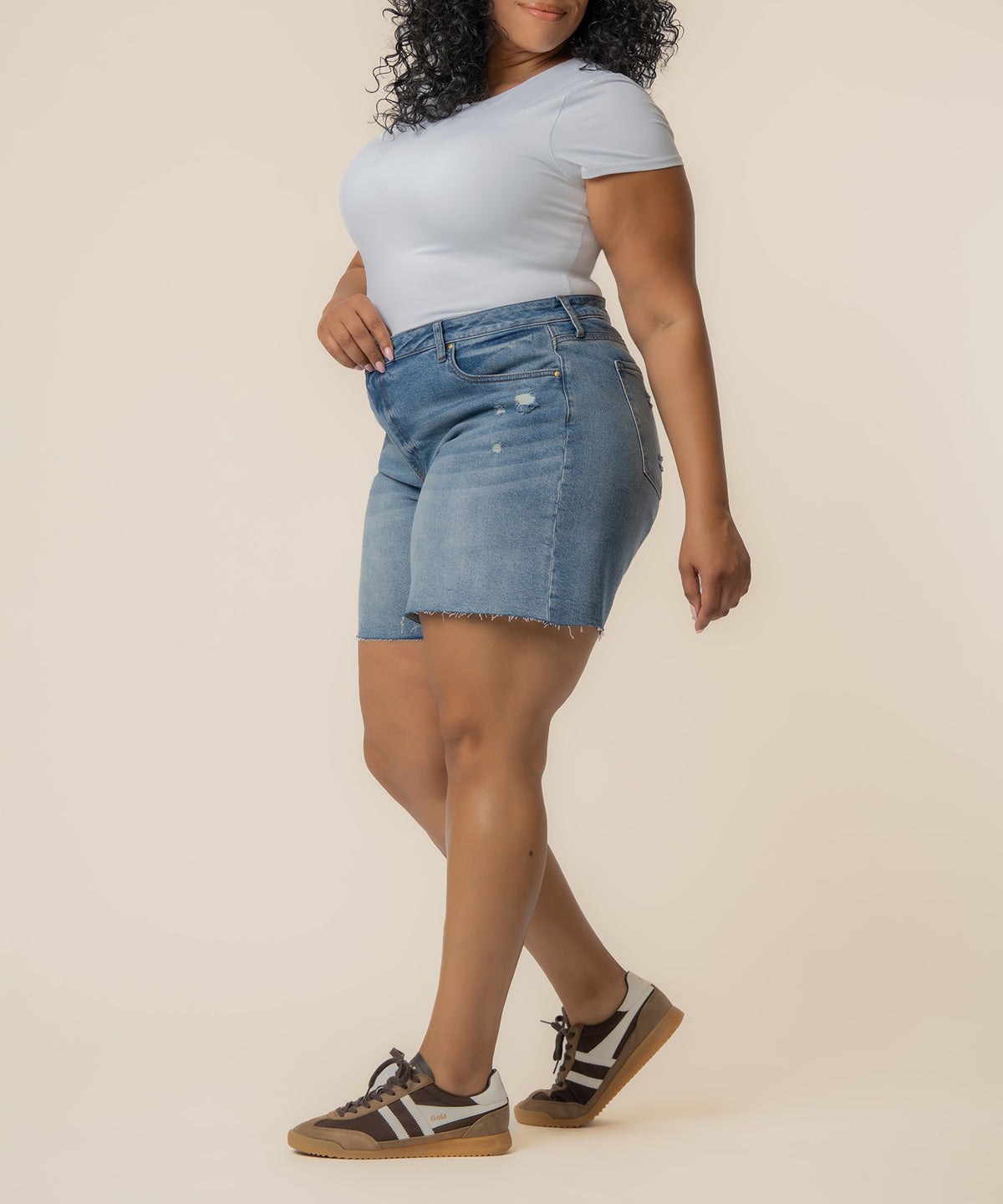 Woman wearing light blue denim Bermuda shorts with distressed detailing and a white short-sleeve shirt.