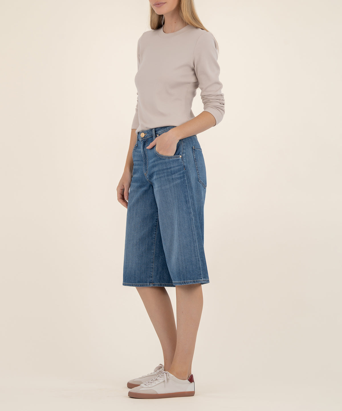 Woman wearing beige long-sleeve top and blue denim bermuda shorts with high waistband and front pockets.