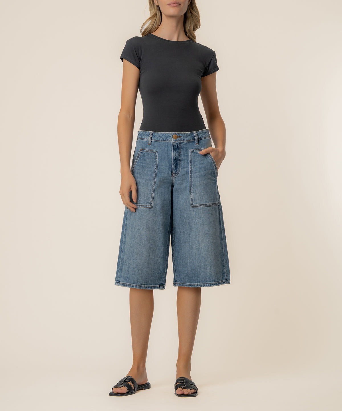 Woman wearing black short-sleeve t-shirt and light blue denim bermuda shorts with patch pockets.