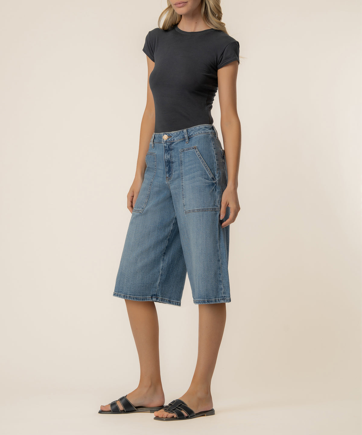 Woman wearing light blue denim bermuda shorts with high rise waistband and cargo pockets, paired with black t-shirt.