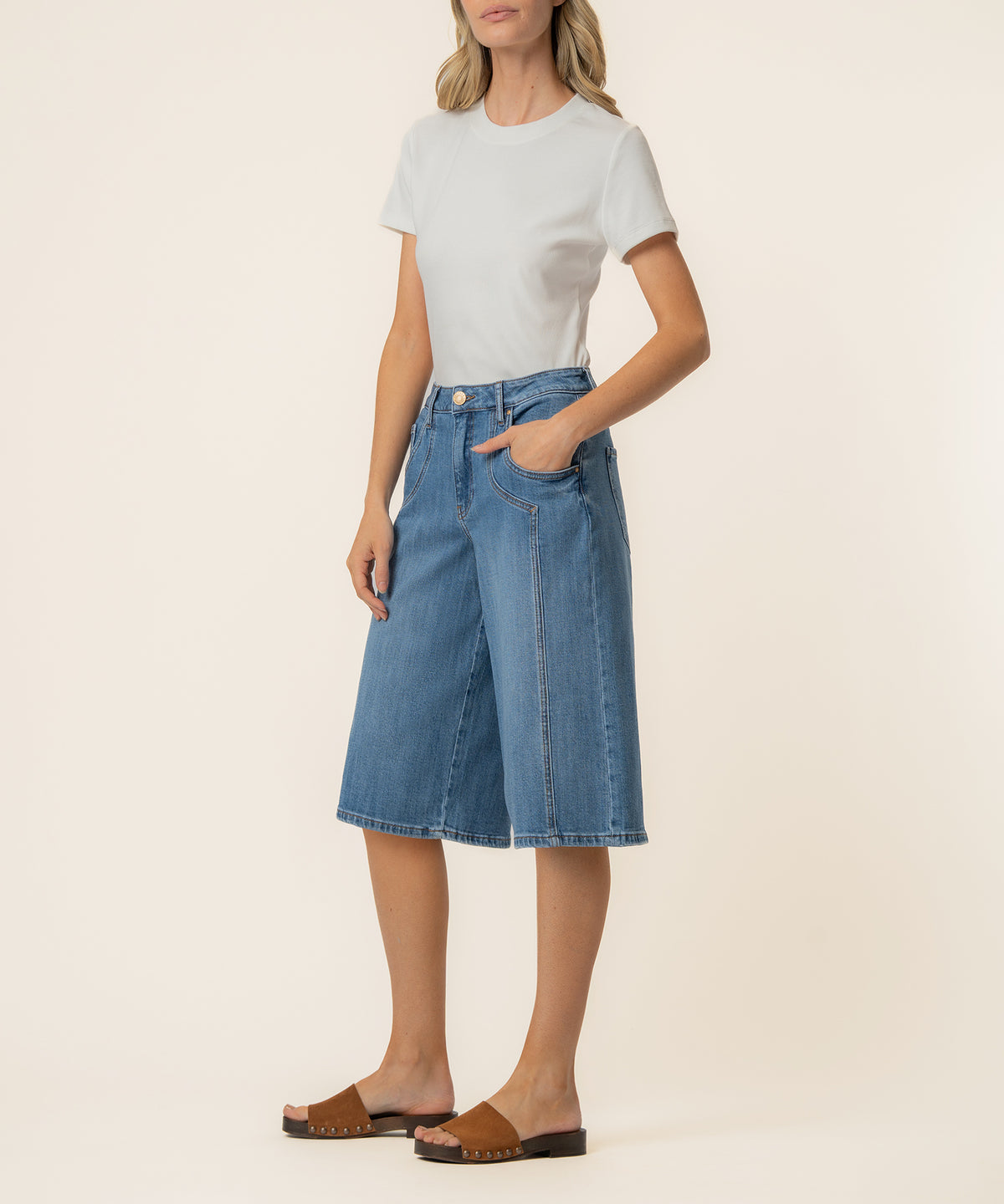 Woman wearing white crew neck t-shirt and blue denim high-rise bermuda shorts with front pockets.