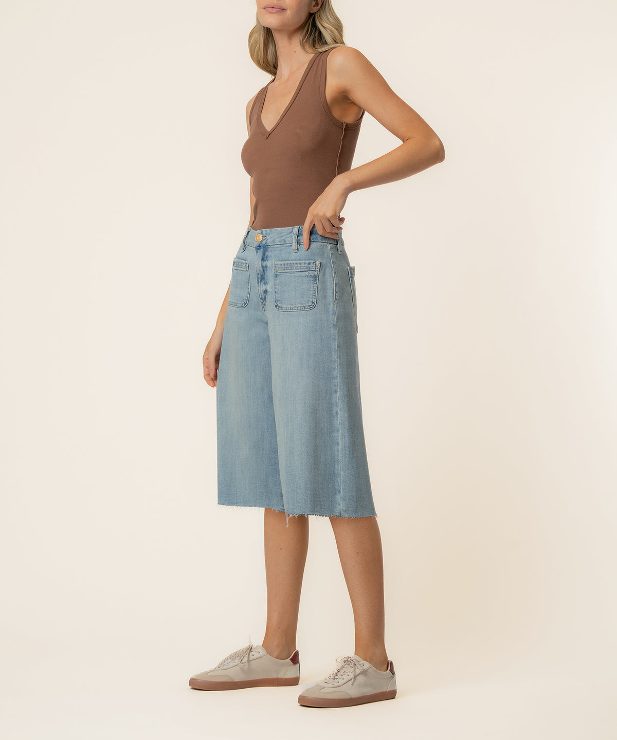 Woman wearing light blue denim bermuda shorts with high rise waistband and brown sleeveless top.