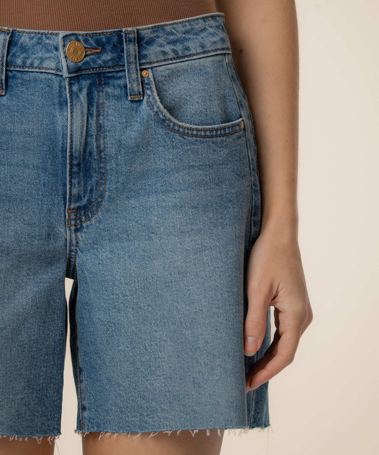 High-rise denim bermuda shorts in light blue wash with raw-cut hem and bronze button closure.