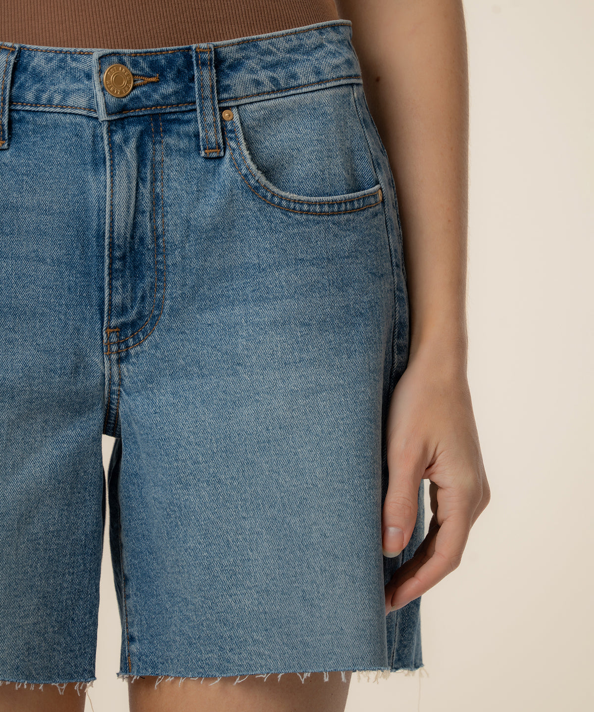 High-rise denim bermuda shorts in light blue wash with raw-cut hem and bronze button closure.