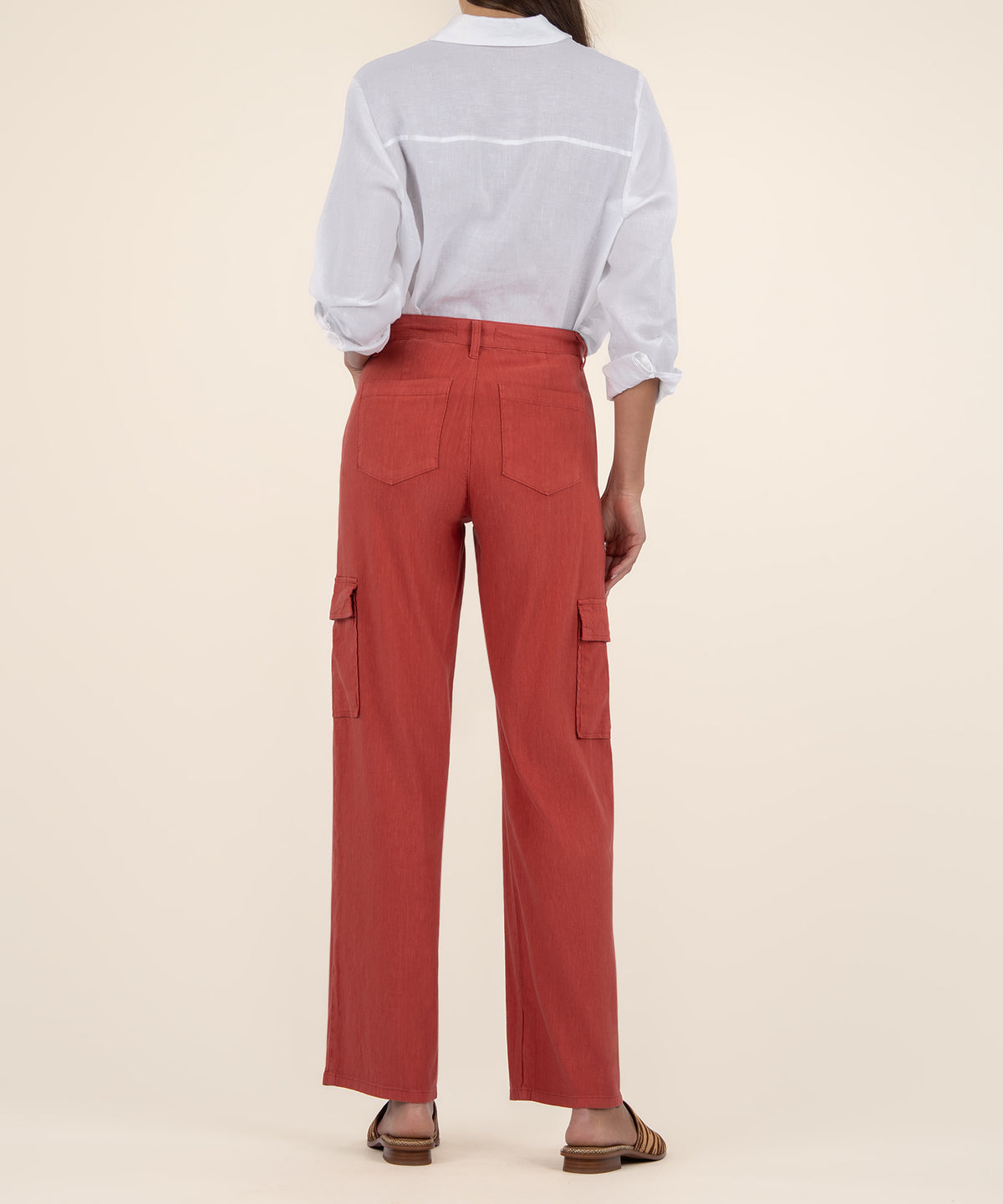 Back view of a person wearing rust-red wide leg cargo pants with a white button-up shirt and brown woven sandals.