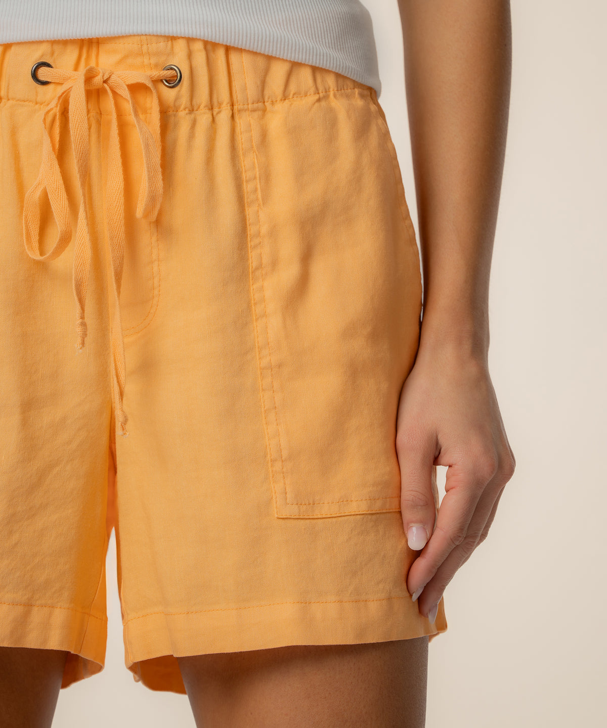 Citrus orange linen shorts with drawstring waist, side pocket, and grommet details.