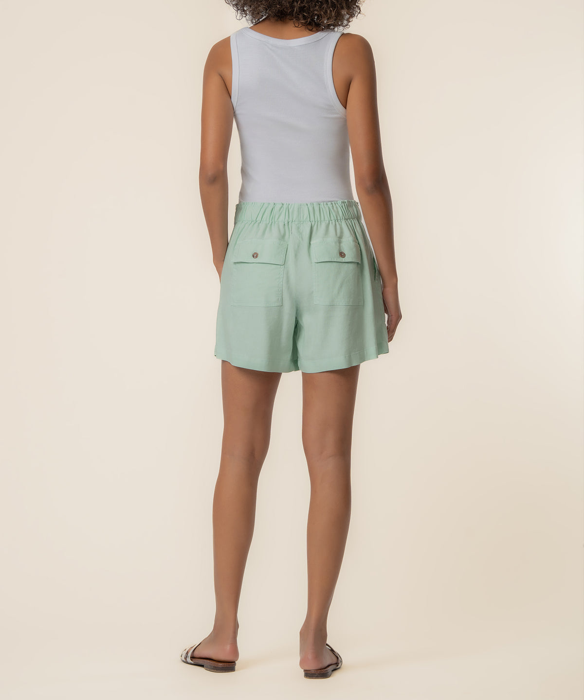 Seafoam green linen drawstring shorts with patch pockets and elastic waistband, shown from back view on model wearing white t