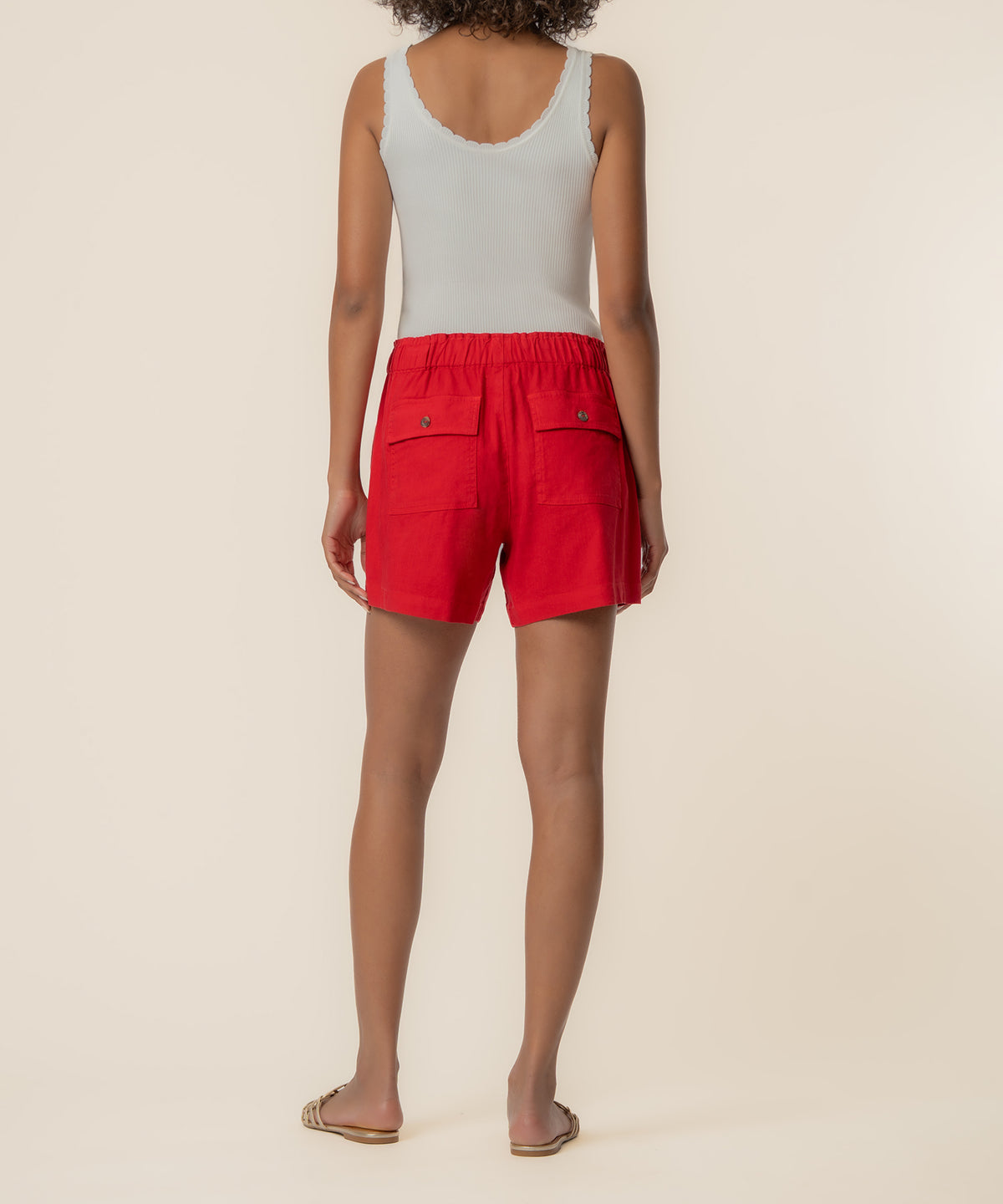 Red linen shorts with elastic waistband and back patch pockets, paired with white ribbed tank top.