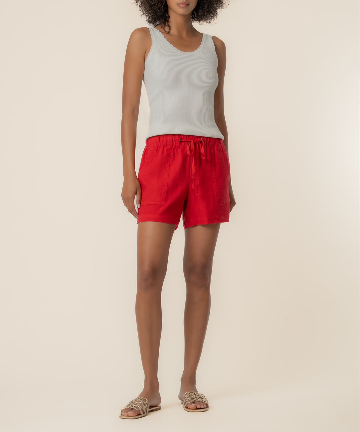 Red linen shorts with drawstring waist and patch pockets, worn with white ribbed tank top.
