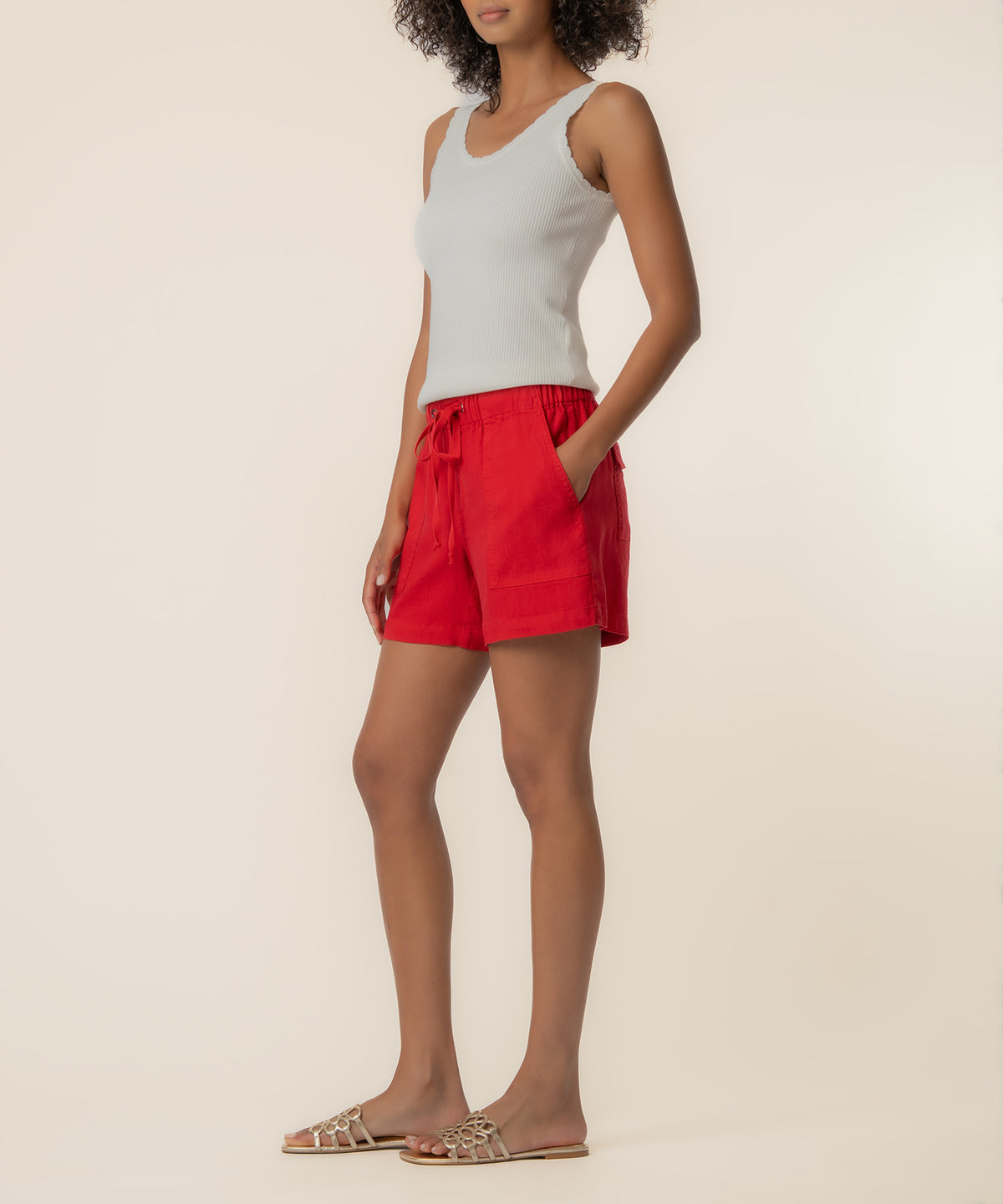 Red linen drawstring shorts with side pockets and elastic waistband, paired with white ribbed tank top.