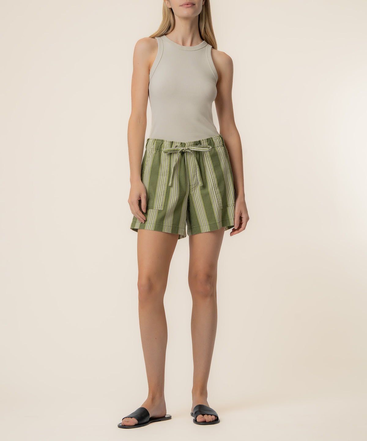 Woman wearing high-rise shorts with olive and ivory vertical stripes and an ivory sleeveless tank top.