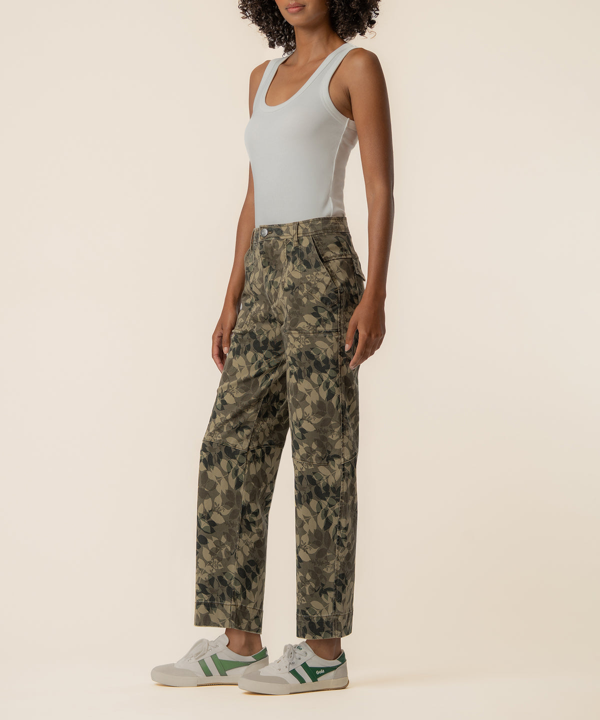 Woman wearing white sleeveless tank top and olive camouflage relaxed-fit pants with green and white sneakers.