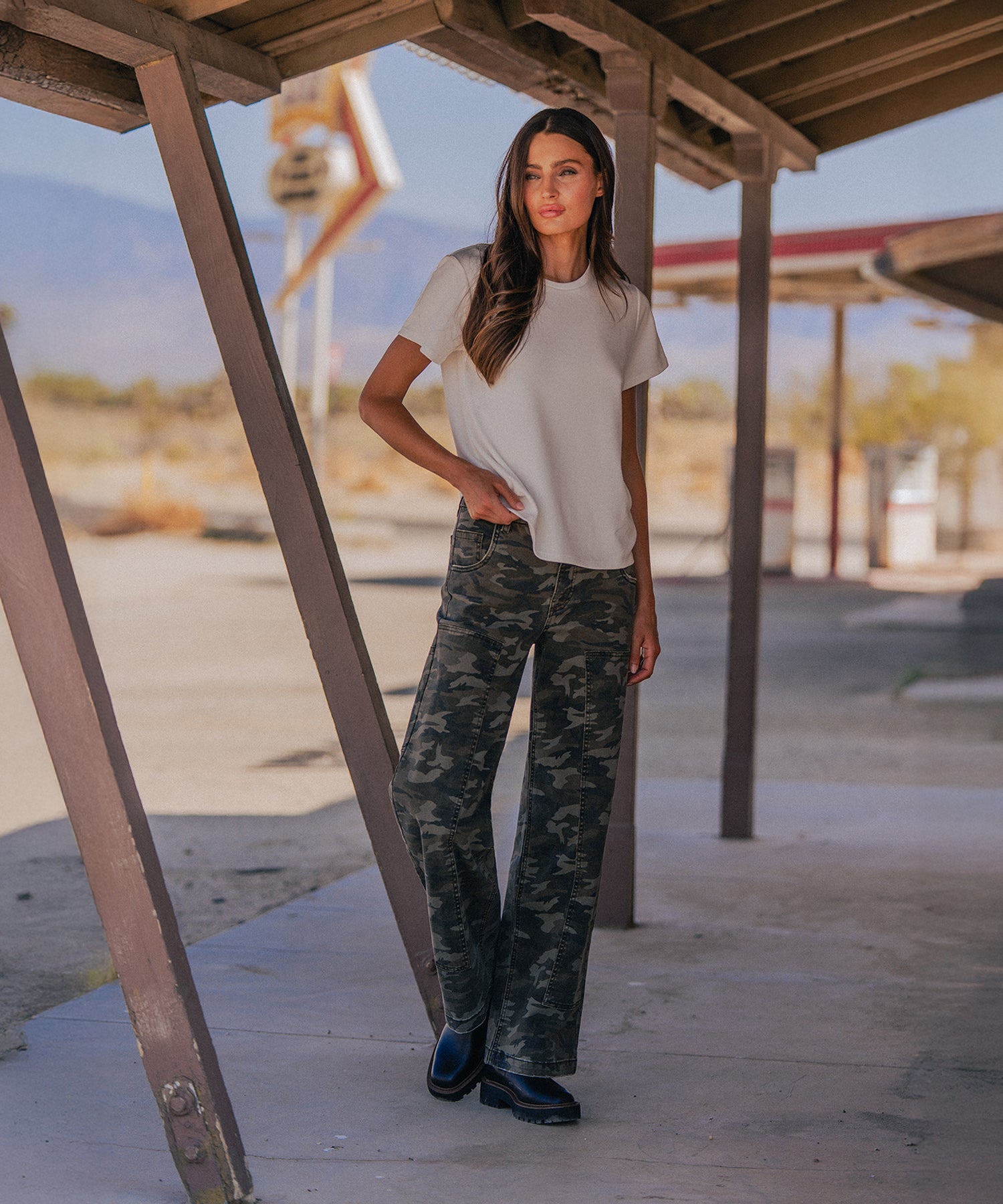 Woman wearing olive camo high-rise wide-leg jeans with a cream t-shirt and black boots.