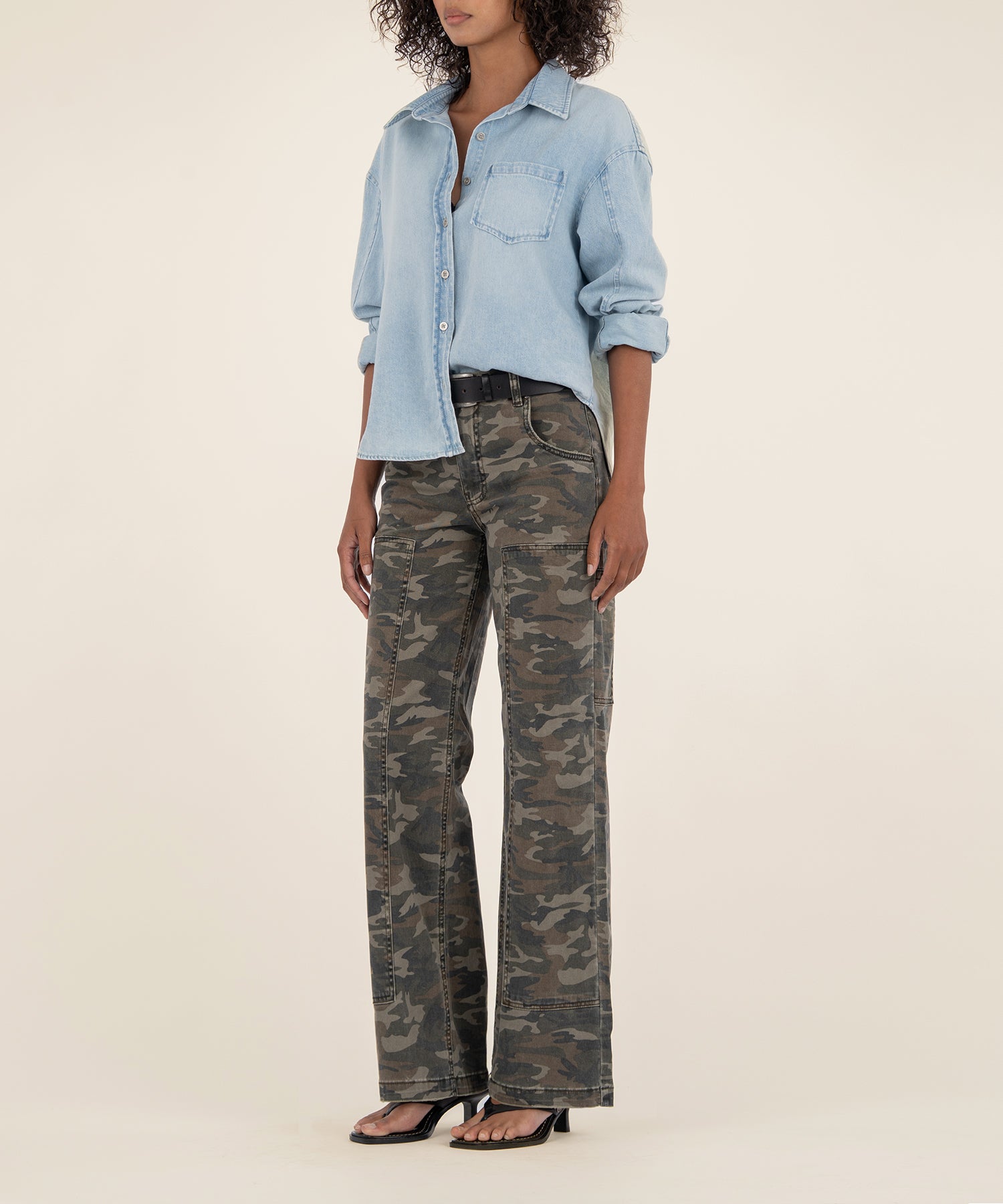 Olive camouflage high-rise wide-leg jeans with cargo pockets worn with light blue denim shirt.