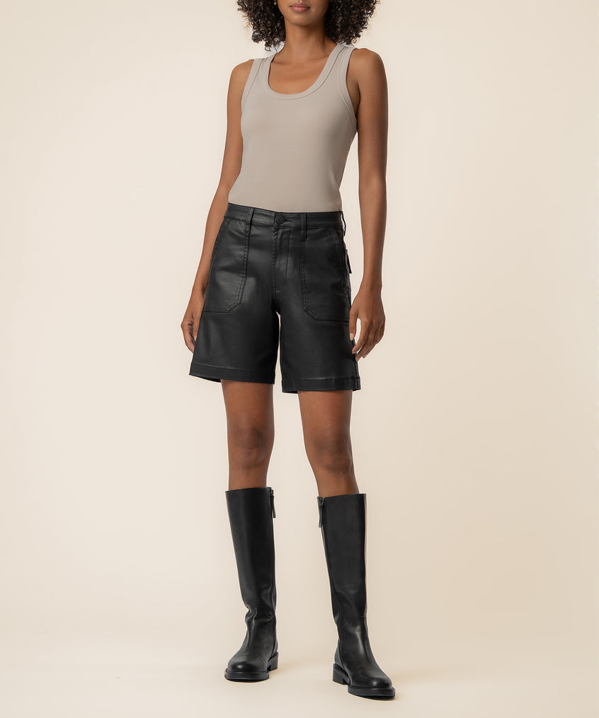 Black coated high-rise bermuda shorts with front pockets, styled with a beige tank top and black knee-high boots.