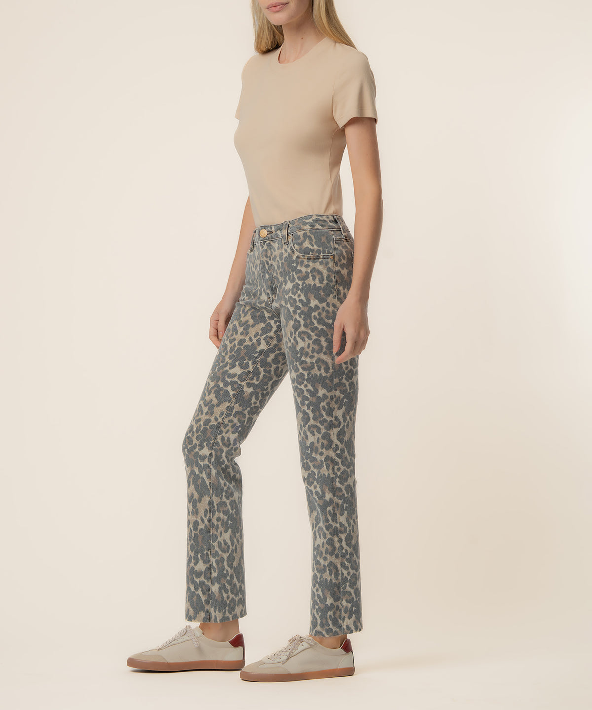 Woman wearing tan short-sleeve t-shirt and leopard print high-rise flare jeans with white sneakers.