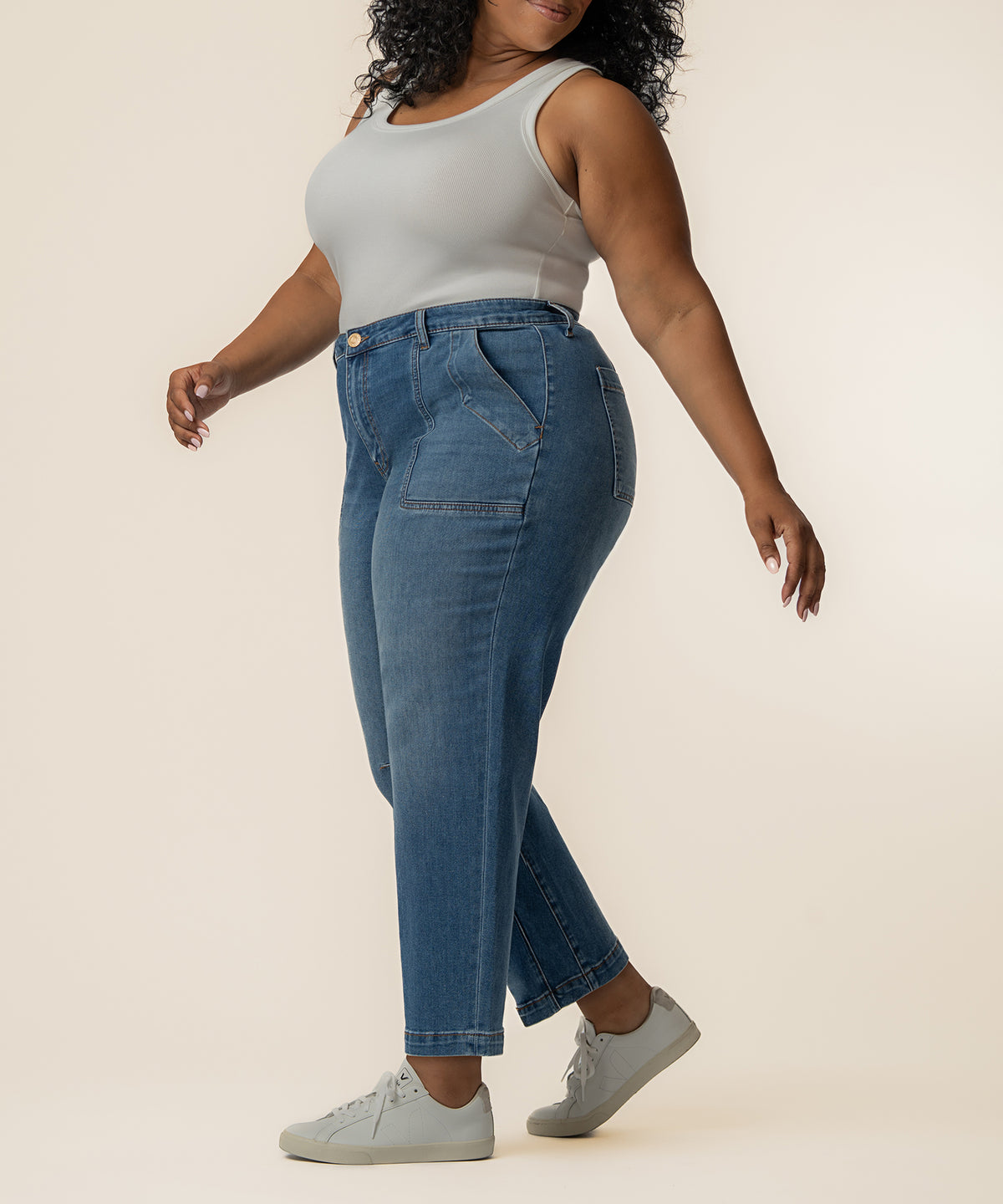 Woman wearing light gray sleeveless tank top and medium-wash blue high-rise relaxed-leg jeans with white sneakers.