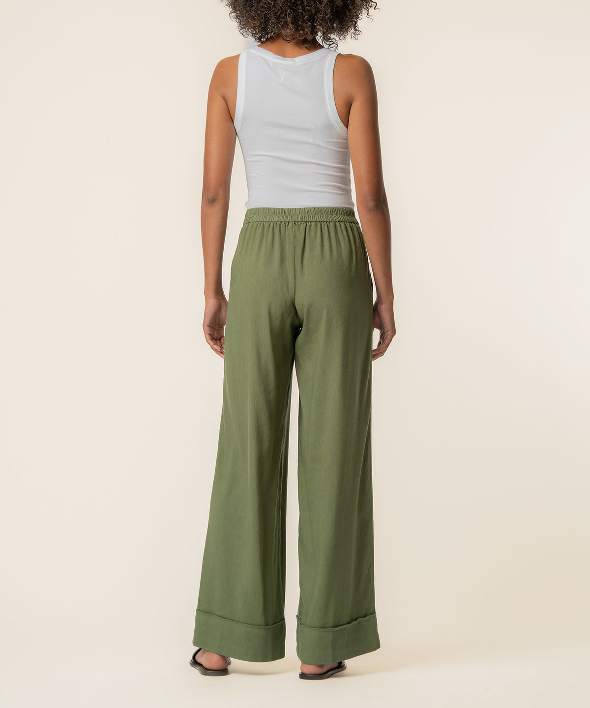 Dill green linen high-rise wide-leg pants with elasticized waistband and cuffed hem, shown on model from waist down.