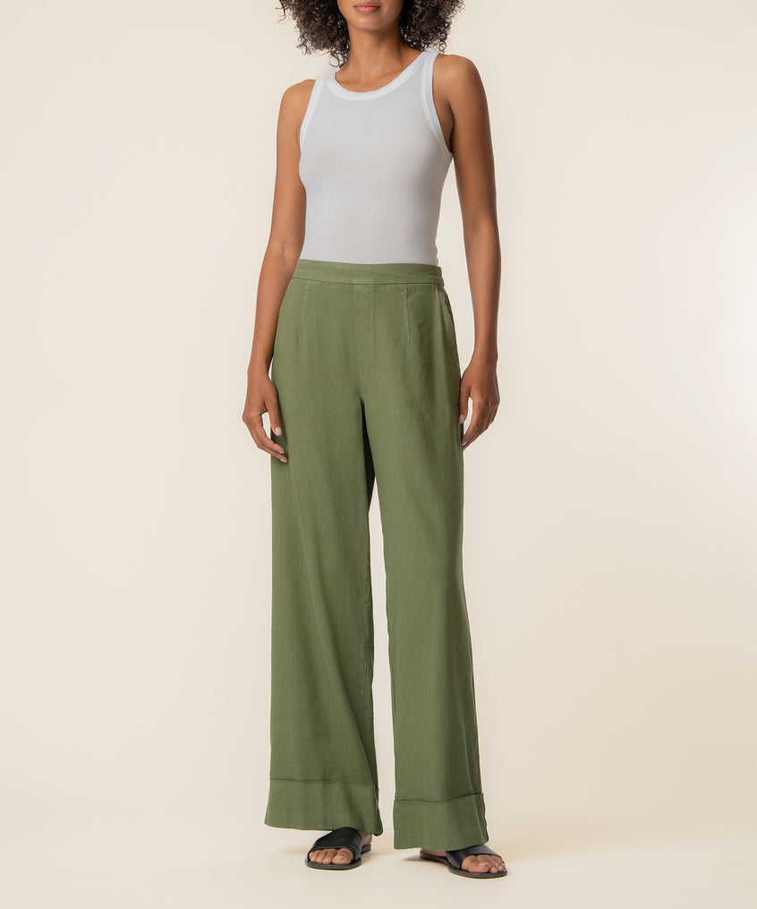 Woman wearing sage green high-rise wide-leg linen pants with cuffed hem and white tank top.