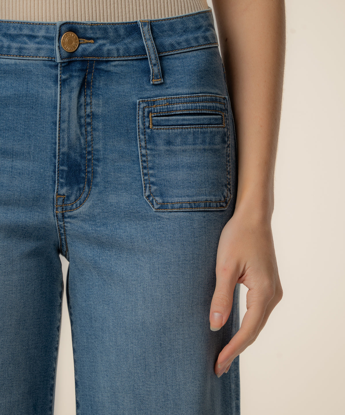 Blue denim wide-leg jeans with high rise waistband, gold button, and patch pockets visible at hip.