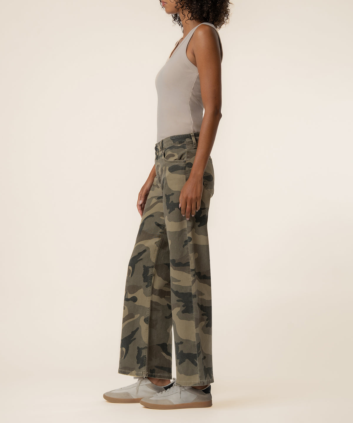 Woman wearing olive camouflage high-rise wide-leg jeans with white tank top and sneakers.