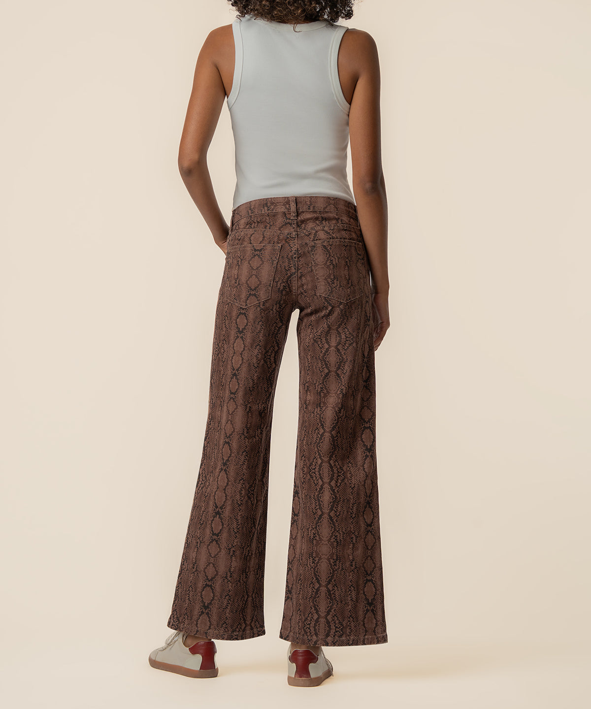 Brown snake-print wide-leg jeans with high rise waistband, shown from back view on model wearing white tank top.