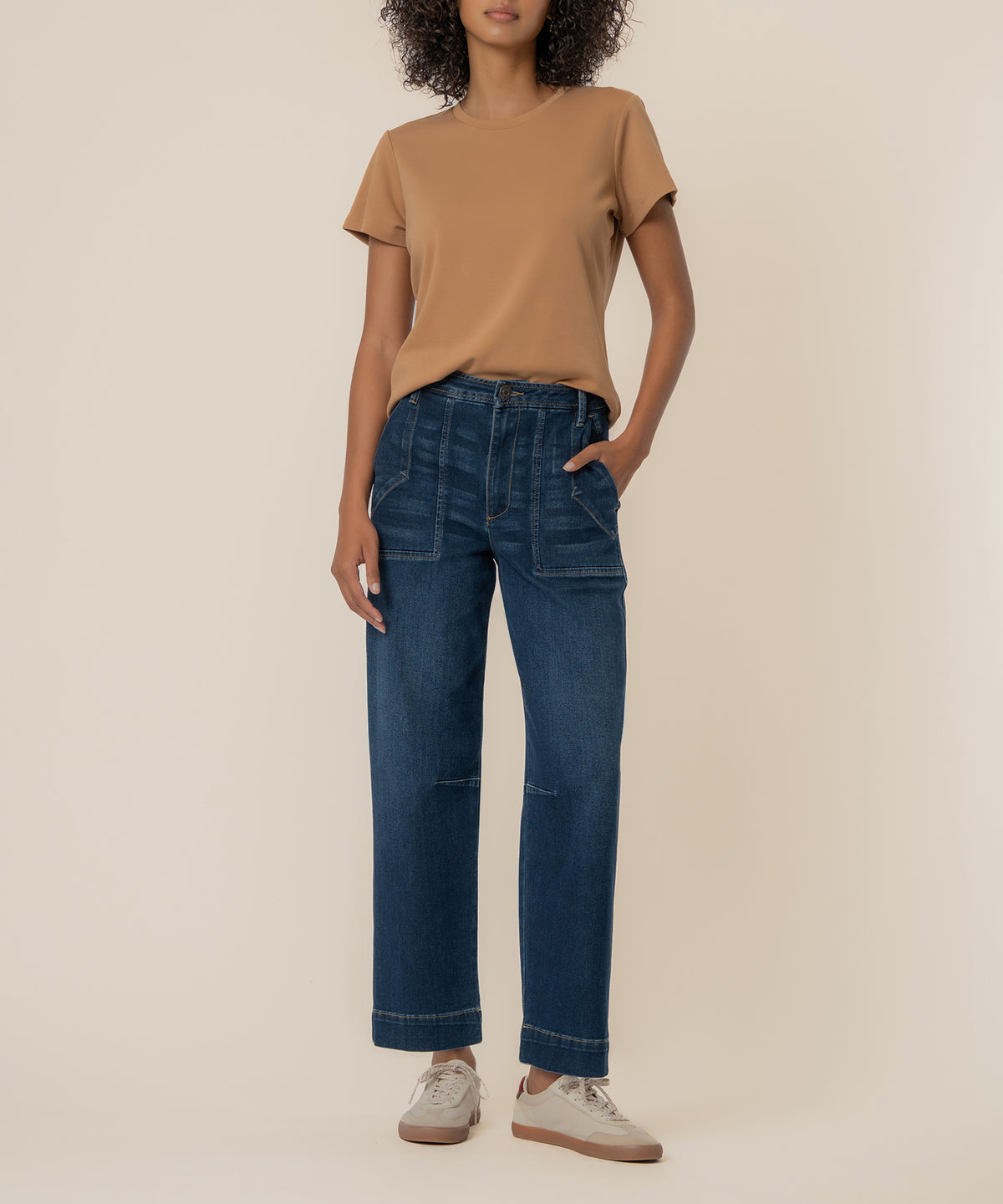 Woman wearing dark wash wide leg barrel jeans with rolled hem and tan short-sleeve t-shirt.