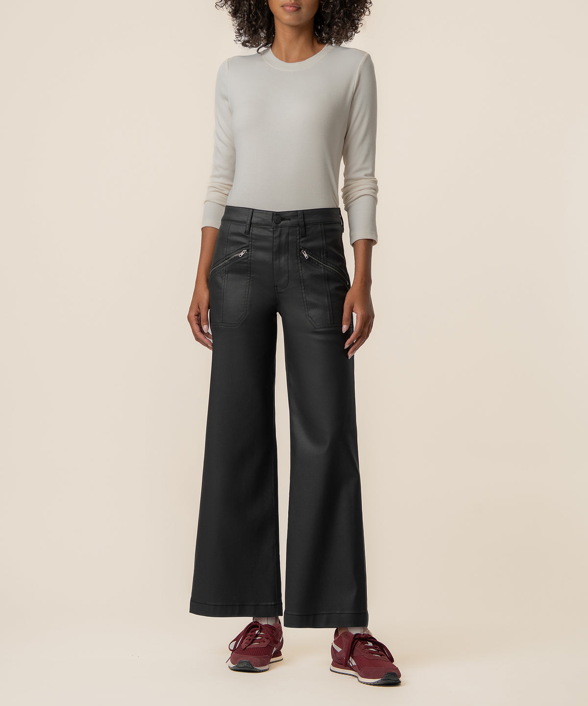 Black coated wide-leg pants with high rise waistband and zip pockets on model wearing cream long-sleeve top.