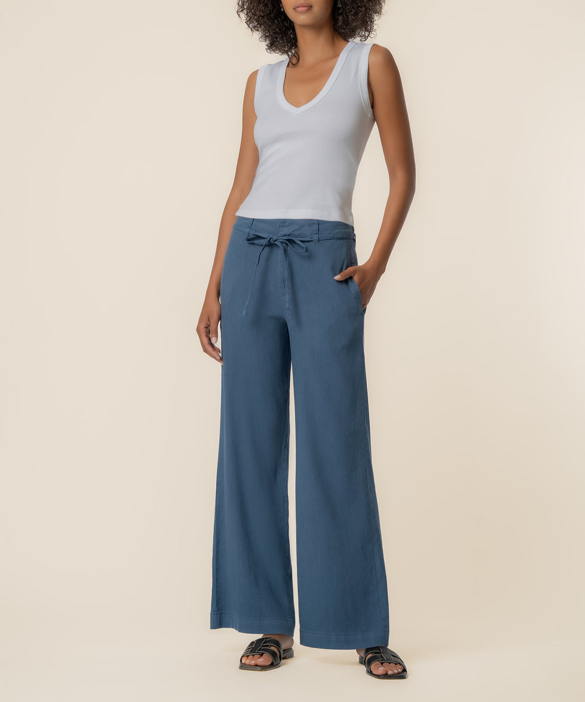 Woman wearing white sleeveless v-neck top and blue wide-leg linen pants with drawstring waist and side pockets.