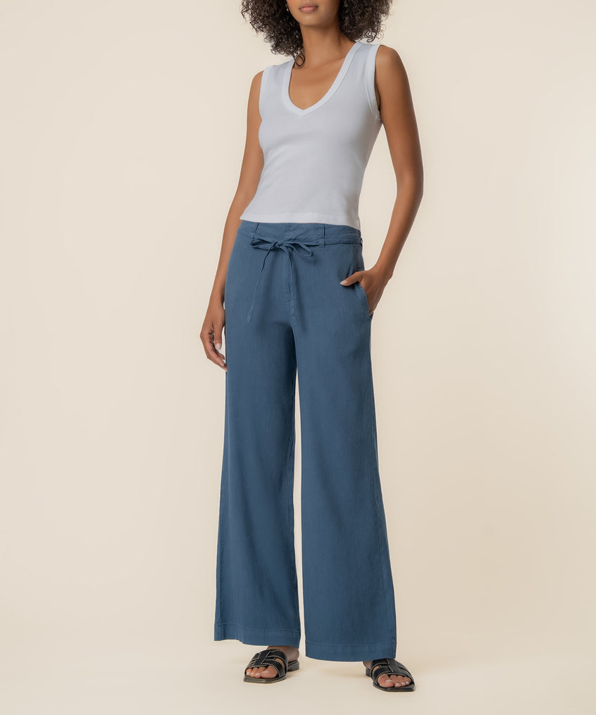Woman wearing white sleeveless v-neck top and blue wide-leg linen pants with drawstring waist and side pockets.
