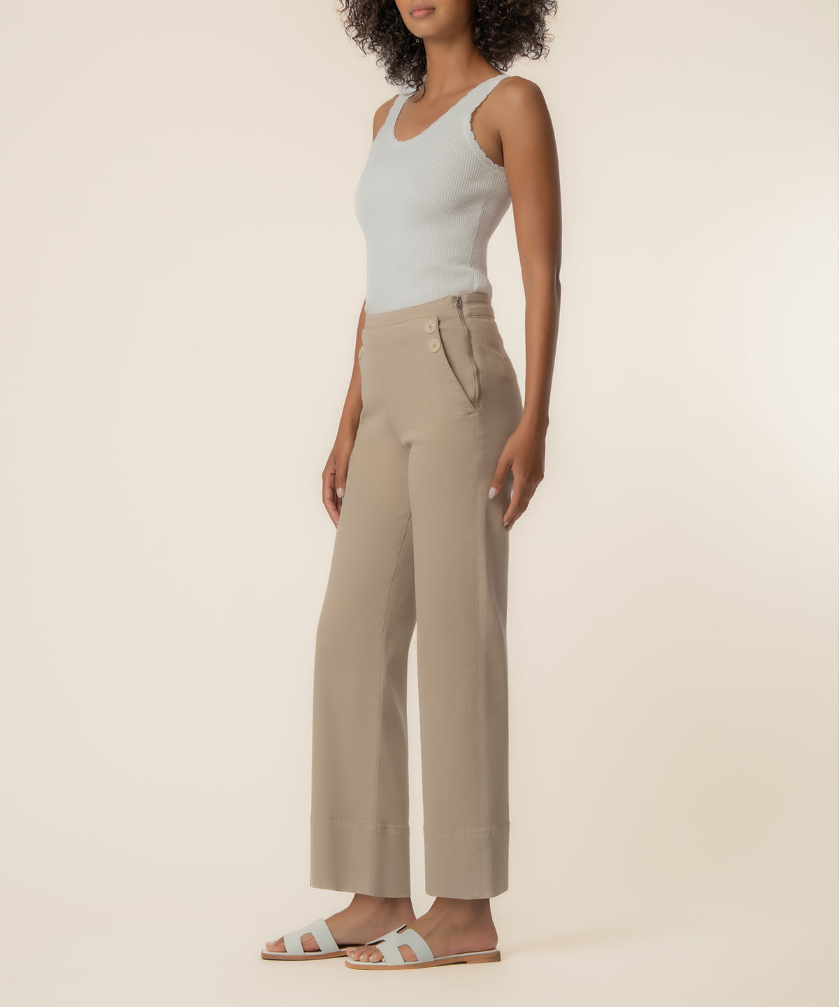 Woman wearing sand-colored high-rise wide-leg twill pants with white sleeveless tank top and white slide sandals.