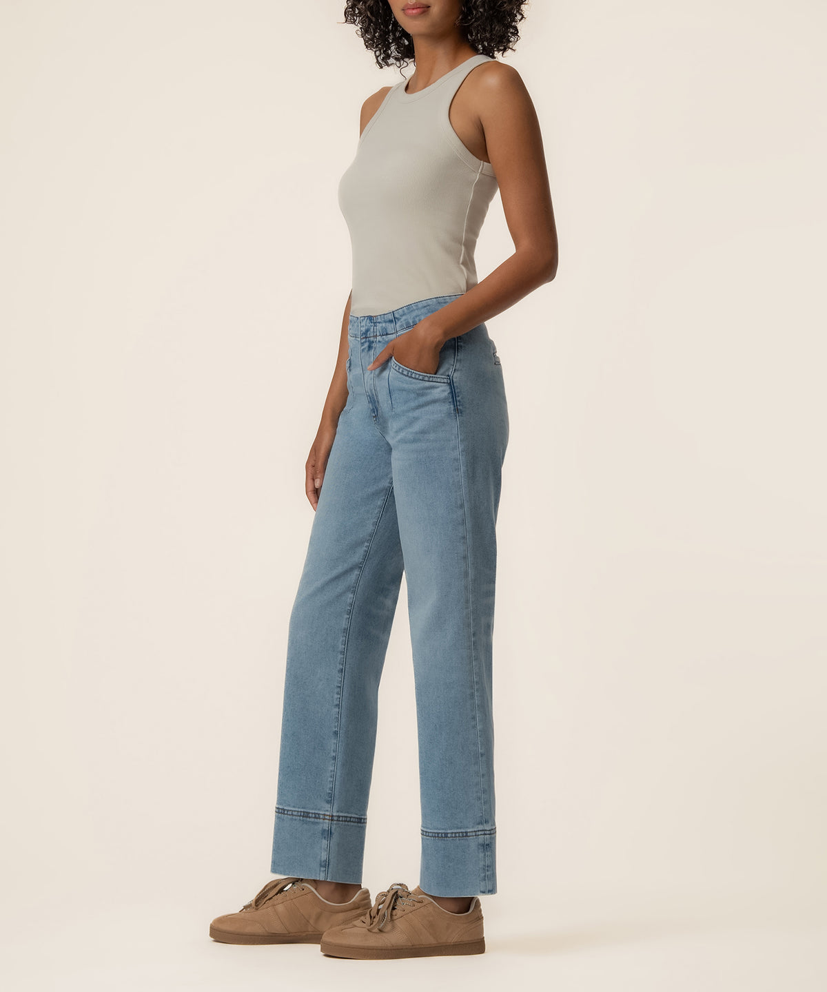 Woman wearing light blue high-rise straight leg jeans with a white sleeveless tank top and tan shoes.
