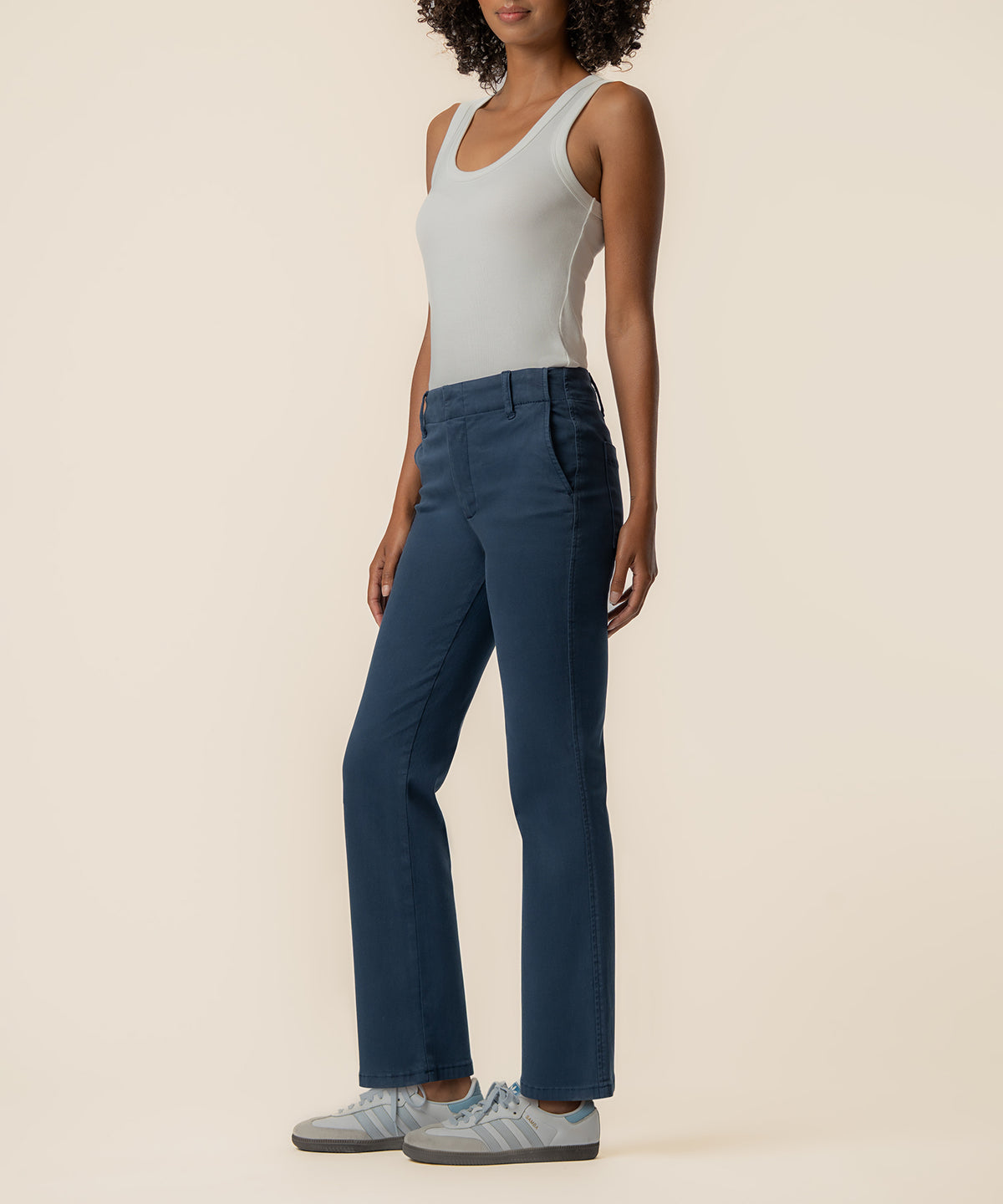 Woman wearing white sleeveless tank top and dark blue high-rise flare trousers with white sneakers.