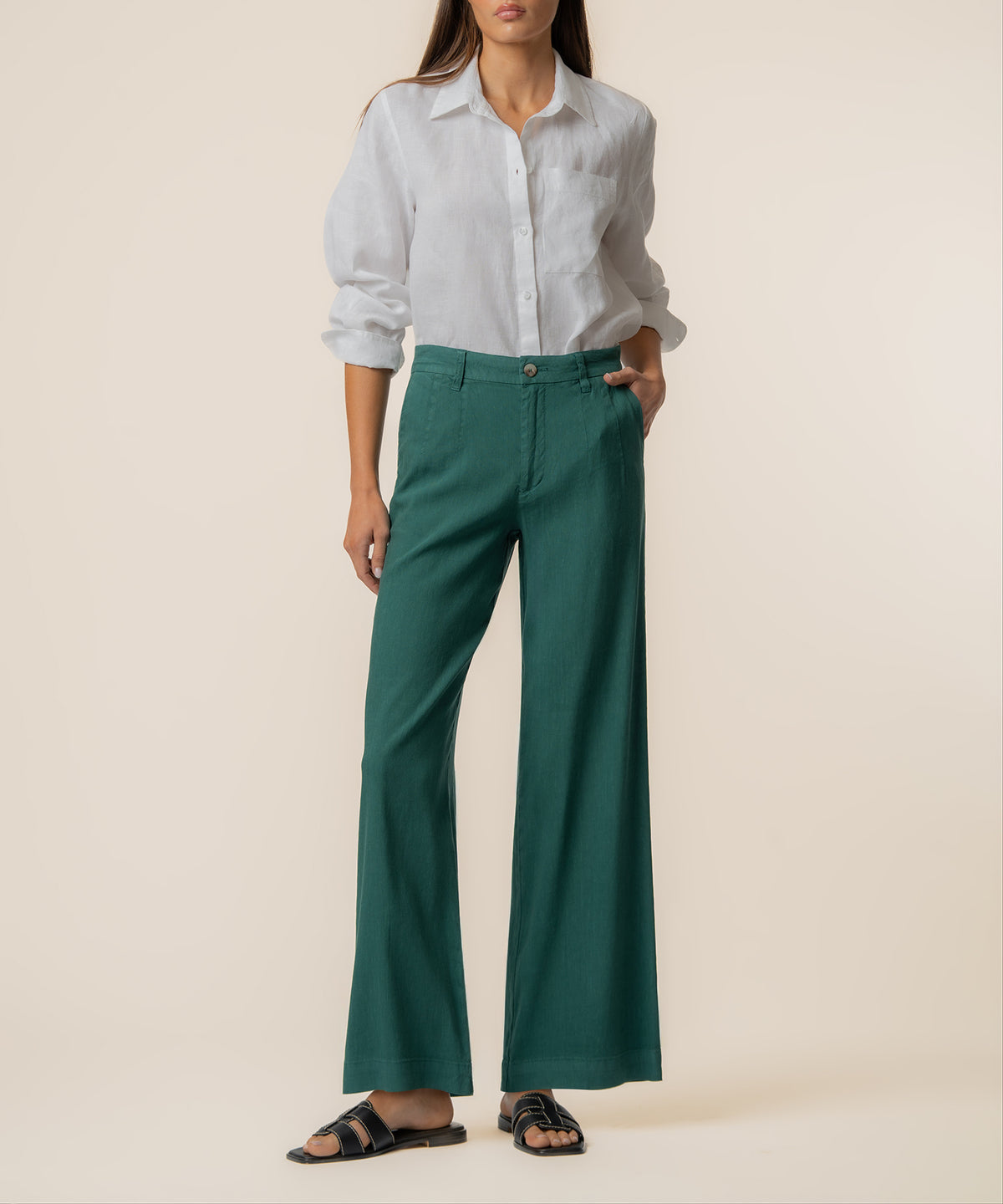 Woman wearing green high-rise wide-leg linen pants with white button-up shirt and black sandals.