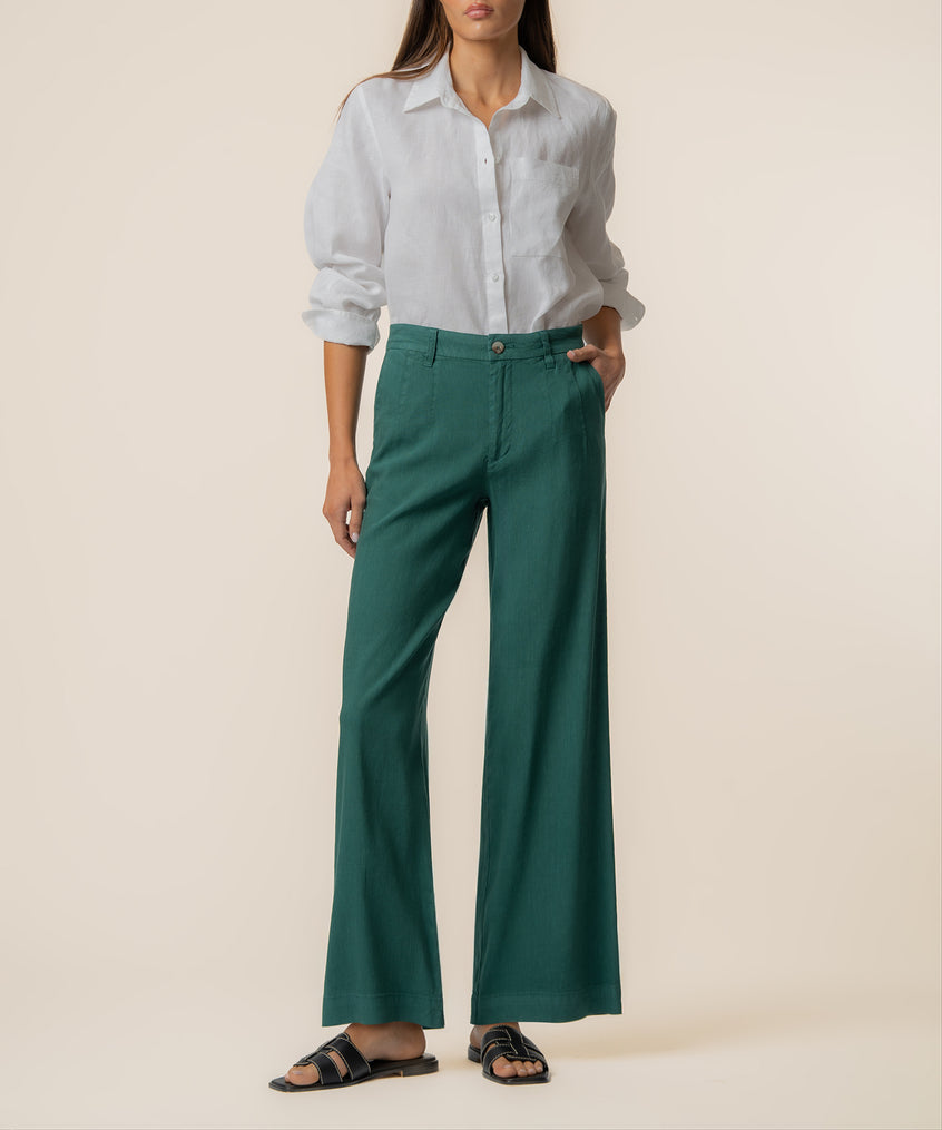 Woman wearing green high-rise wide-leg linen pants with white button-up shirt and black sandals.
