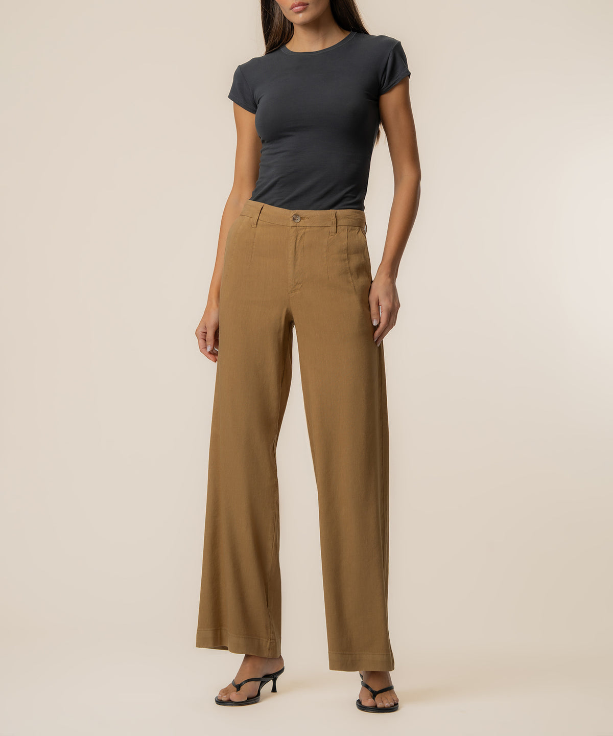 Woman wearing tan linen high-rise wide-leg pants with black short-sleeve shirt and black sandals.