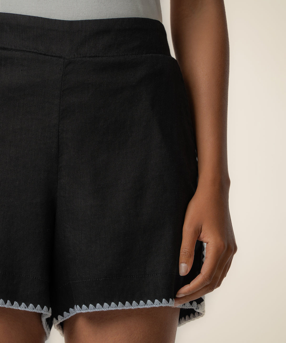 Black linen bermuda shorts with white contrast stitching at the hem, shown on model from waist down.